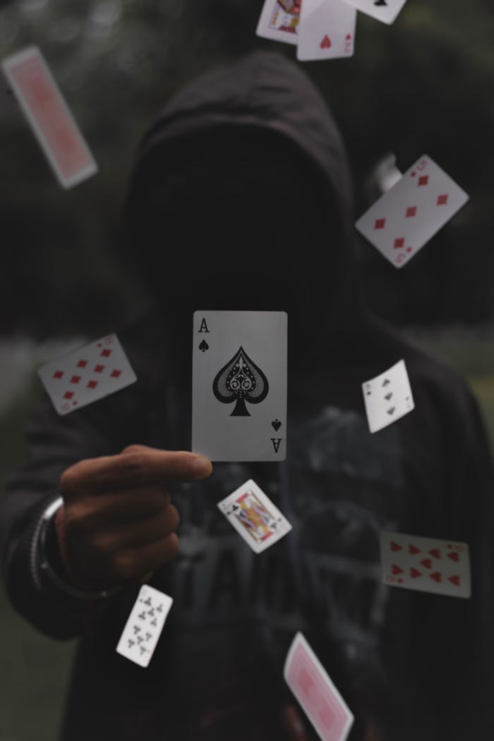 Enigmatic hooded figure with playing cards floating in mid-air, focusing on the ace of spades.